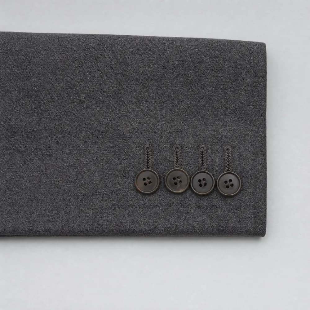 A jacket cuff laid flat with four buttons set close together along the sleeve vent.