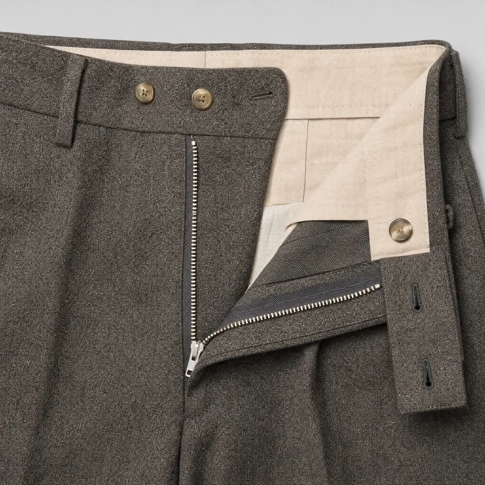 A metal zip fly on wool trousers laid flat, the teeth catching the light.