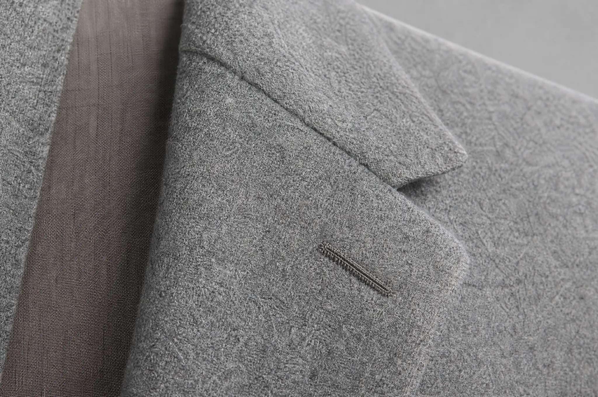 Macro view of the roll line of a notched lapel in grey flannel, with a worked buttonhole.