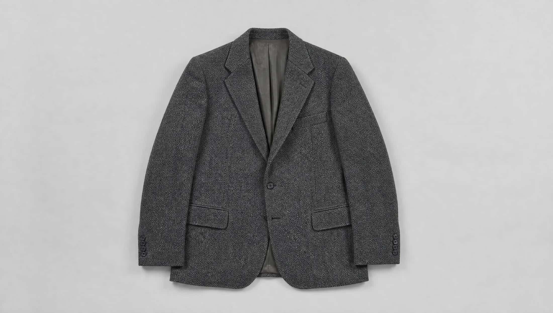 A single-breasted charcoal herringbone jacket laid flat and symmetrical, photographed from directly above.