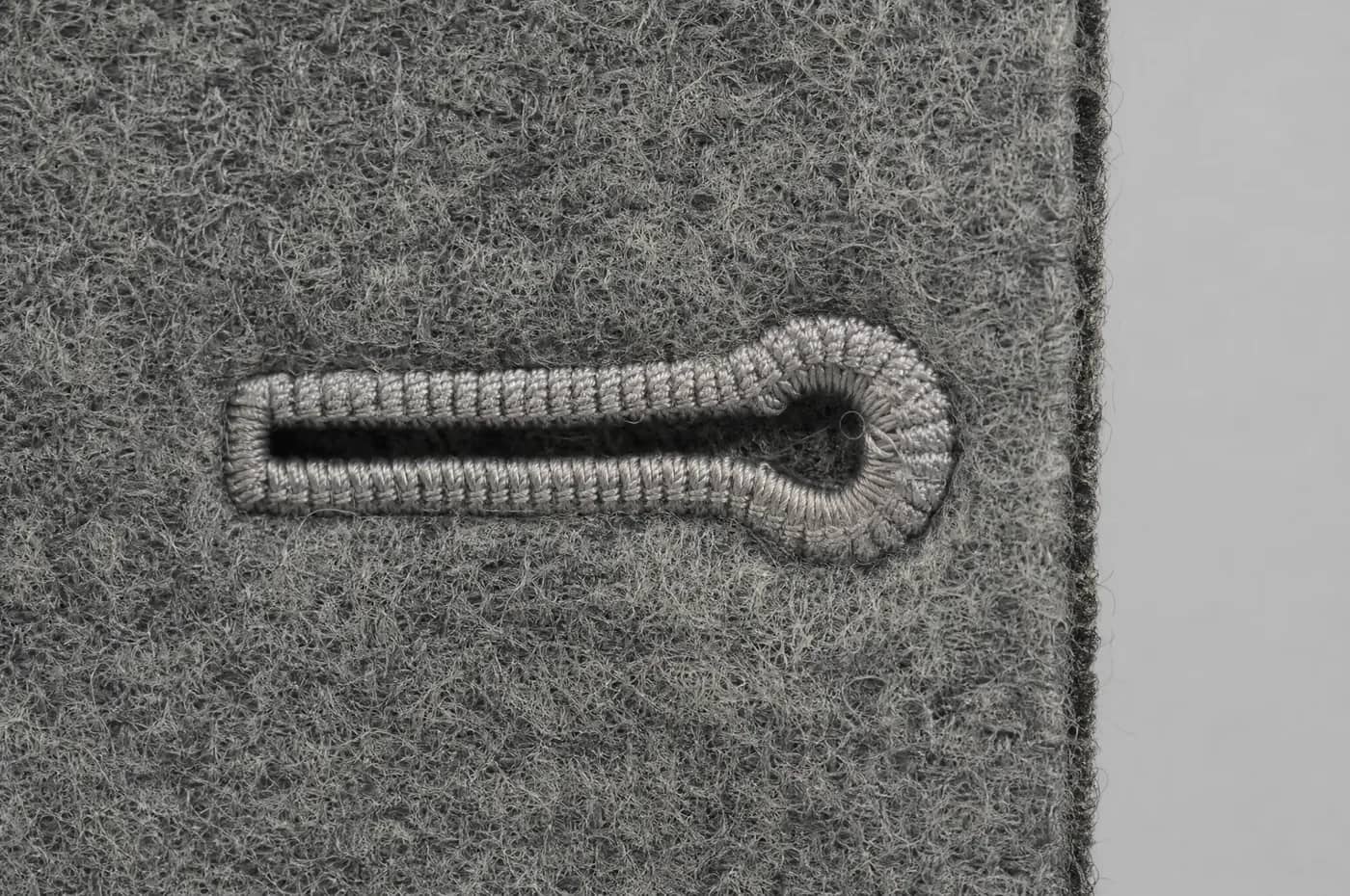 Macro view of a hand-worked buttonhole in grey wool, showing the gimp and purl stitches.